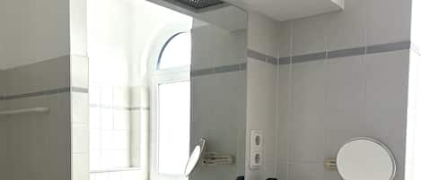Casa de banho com um espelho grande, uma pia com torneira, um dispensador de toalhas e um copo de água no balcão.