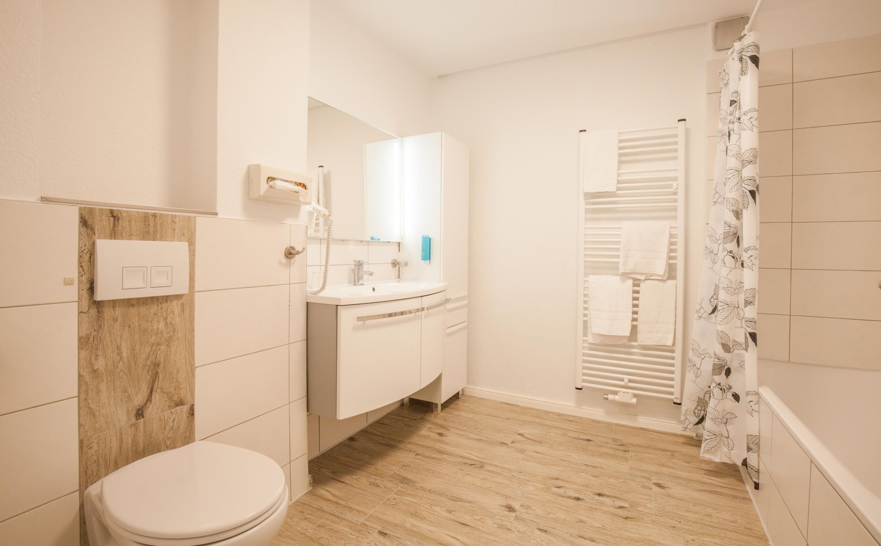 A bathroom with a toilet, sink, mirror, towel rack, and shower curtain.