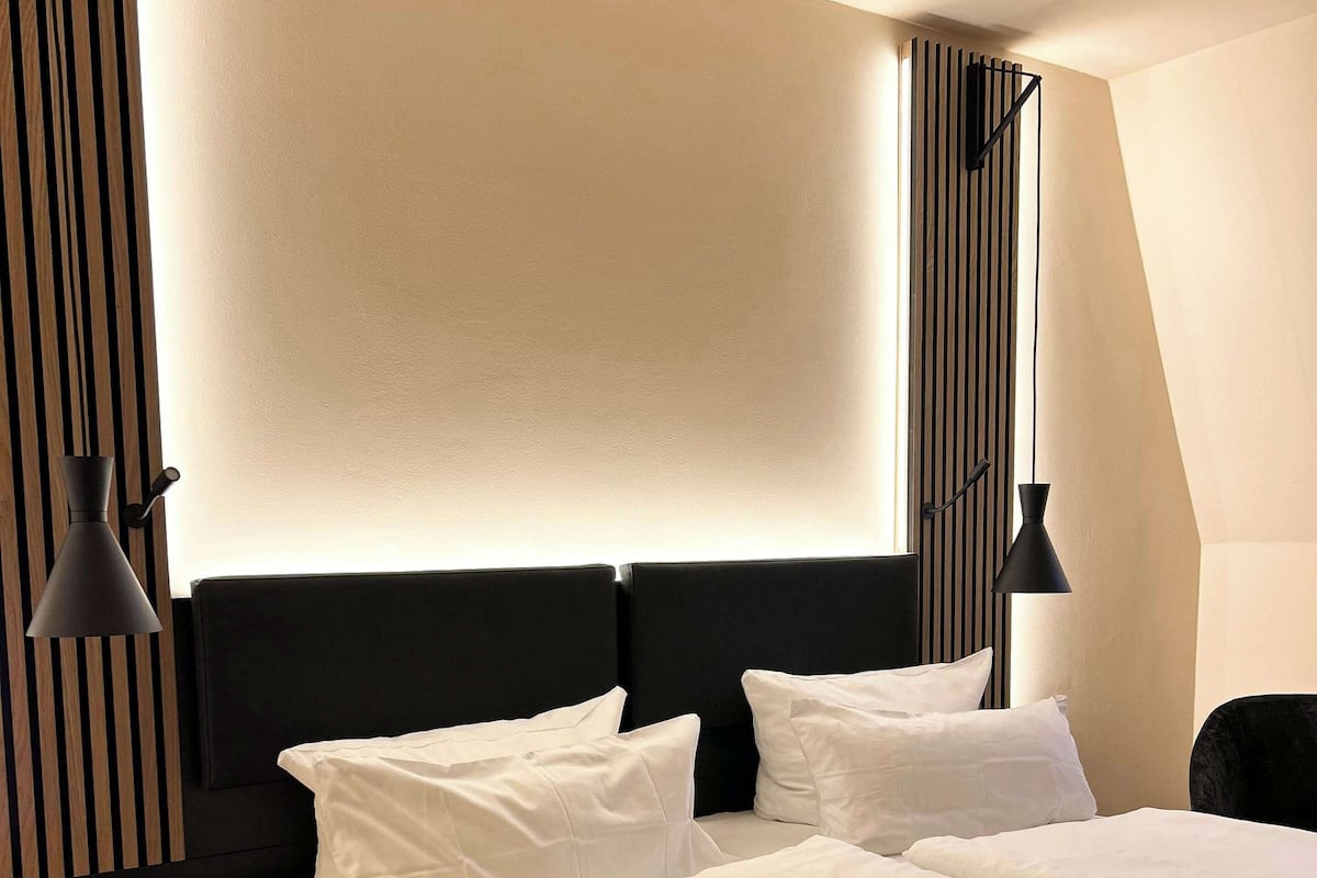 Una habitación de hotel moderna con una cama grande, dos mesitas de noche y un cabecero con líneas verticales.