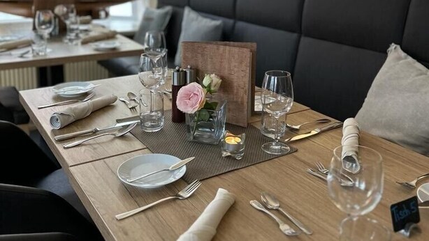 Un comedor con una mesa de madera dispuesta para una comida, un sofá tapizado de color negro y una pared decorada con cuadros.