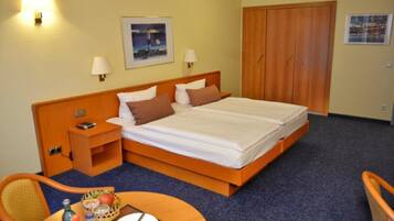 Habitació d'hotel amb un llit gran, dues làmpades de nit, una petita taula de nit, un armari de fusta, un quadre encimbellat a la paret i una taula petita amb una cadira.