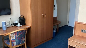 A hotel room with a wooden wardrobe, a desk with a chair, a bed, and a television on the wall.
