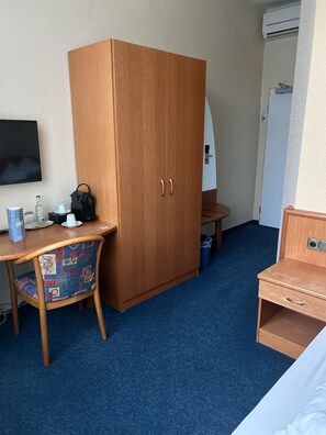 A hotel room with a wooden wardrobe, a desk with a chair, a bed, and a television on the wall.
