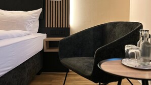 Une chambre d’hôtel moderne, équipée d’un lit, d’une chaise, d’une petite table avec des verres et d’une lampe fixée au mur.