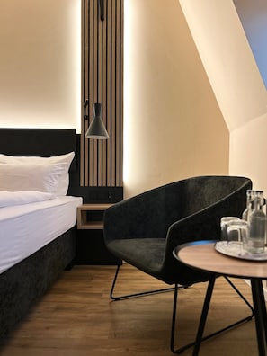 Une chambre d’hôtel moderne, équipée d’un lit, d’une chaise, d’une petite table avec des verres et d’une lampe fixée au mur.