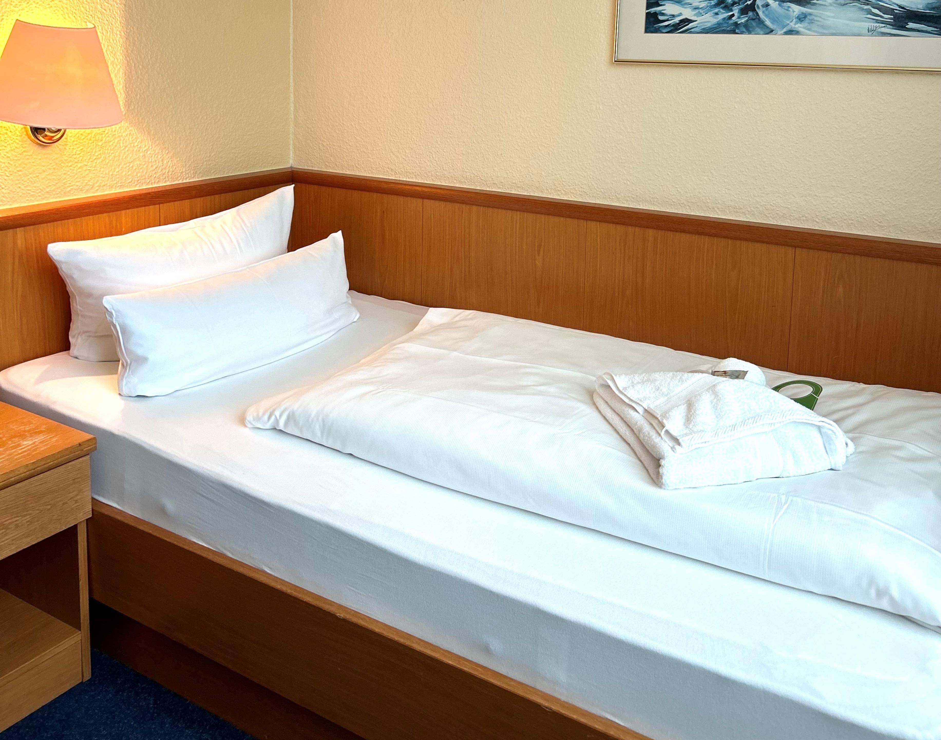 A neatly made bed with white linens, a wooden headboard, and a lamp on the nightstand.