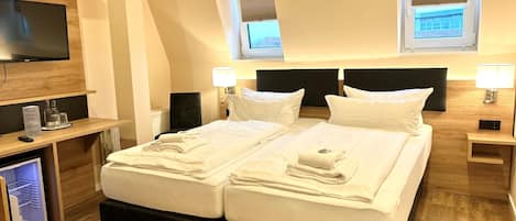 A hotel room with a bed, bedside tables, a TV, and a desk with a computer and glasses.
