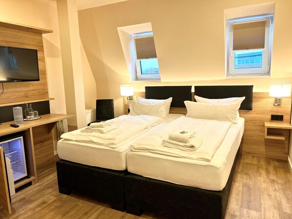 A hotel room with a bed, bedside tables, a TV, and a desk with a computer and glasses.