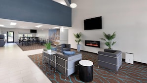 A spacious lobby with a high ceiling, a flat-screen TV mounted on the wall, a fireplace, and several seating areas with modern furniture. - Baymont by Wyndham Moss Point/Pascagoula (Moss Point)