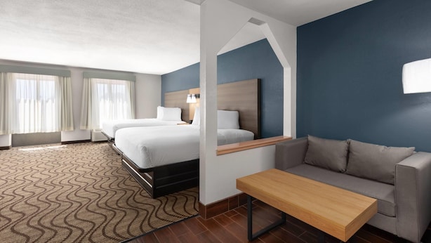 A hotel room with a bed, a sofa, a table, and a mirror. - Baymont by Wyndham Moss Point/Pascagoula (Moss Point)