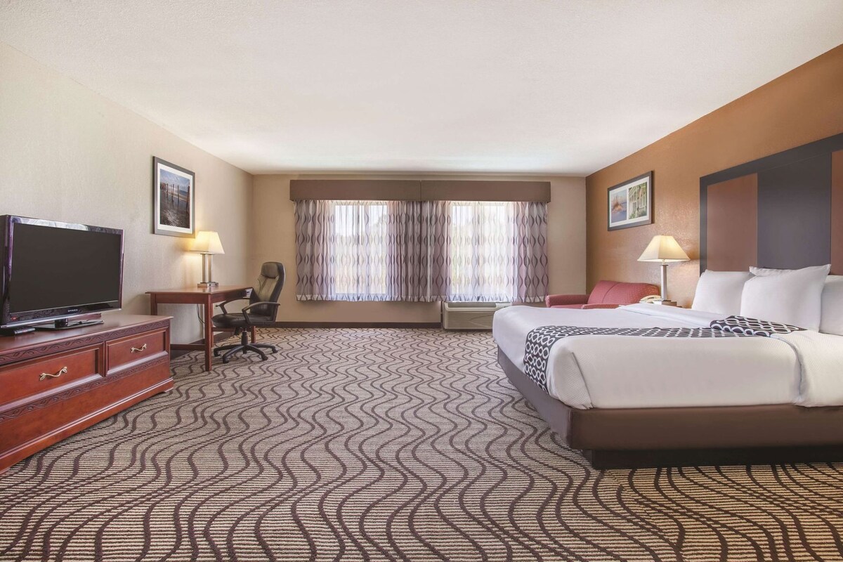 A hotel room with a bed, a TV, a desk, a chair, and a window with curtains.