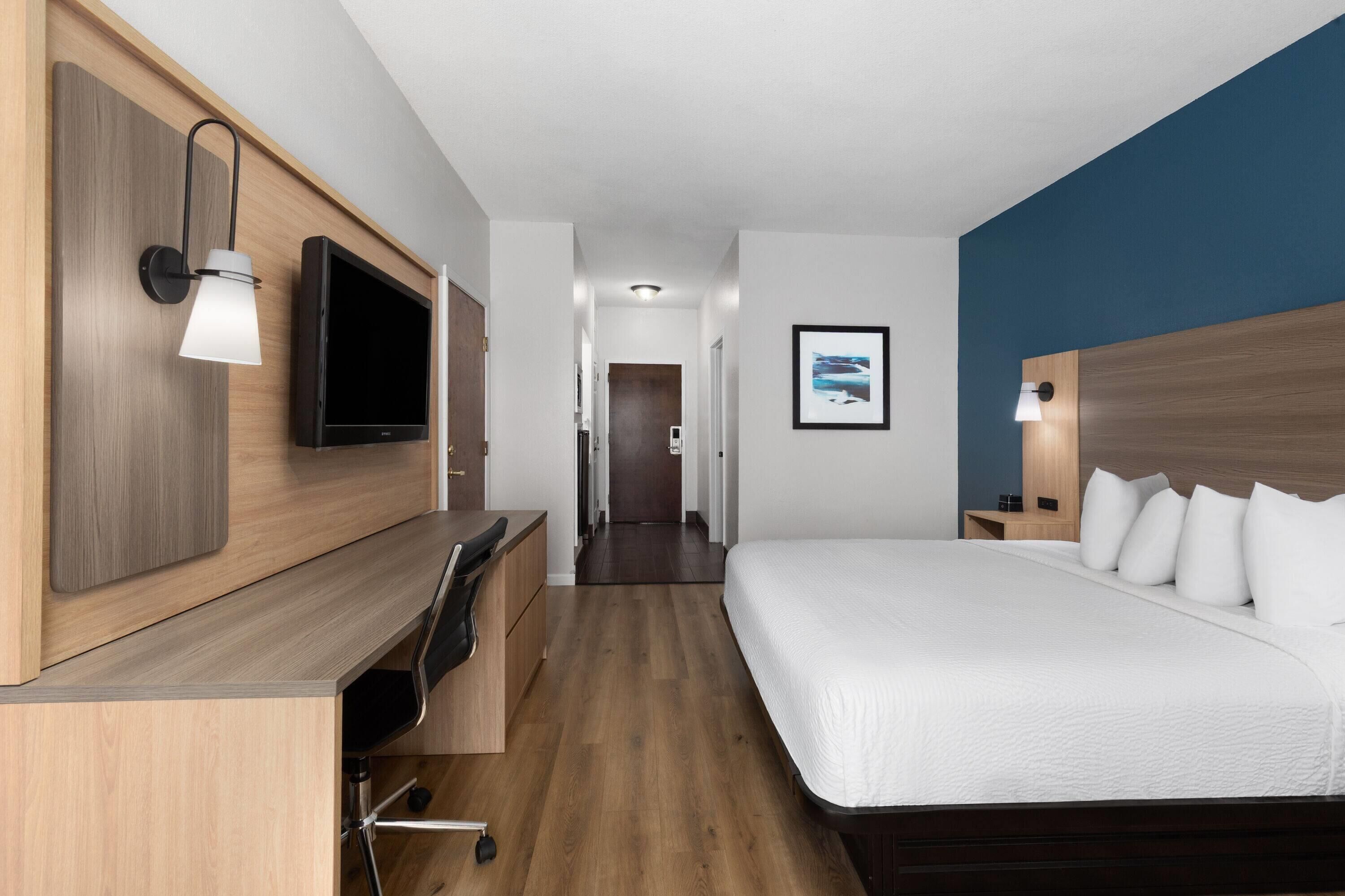 A hotel room with a bed, desk, chair, TV, and wall-mounted lamps.