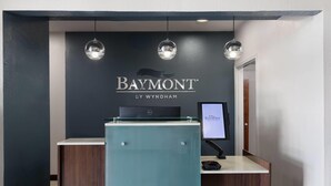 A reception desk with a dark wall, a glass partition, and a computer monitor. - Baymont by Wyndham Moss Point/Pascagoula (Moss Point)