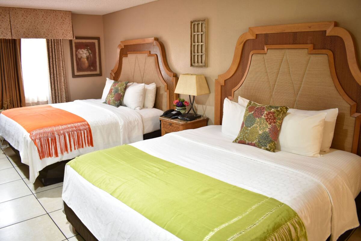 Two double beds with wooden headboards, a nightstand with a lamp, and a framed picture on the wall.