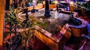 A nighttime view of a hotel courtyard with a fountain, potted plants, and a well-lit balcony. - Hotel Baja San Diego - A Boutique Hotel (San Ysidro)