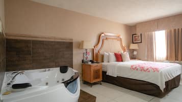 A hotel room with a large bathtub, a double bed with a wooden headboard, and a nightstand with a lamp.