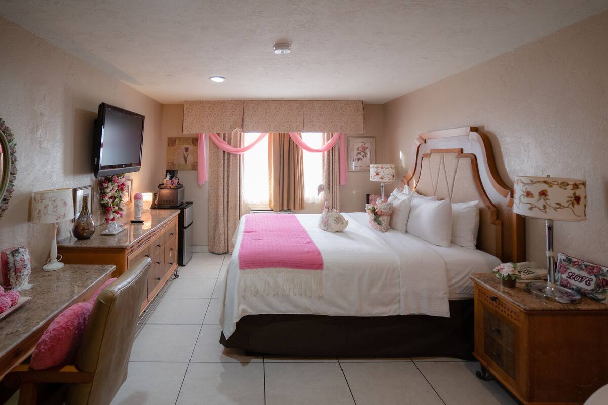 A hotel room with a bed, bedside table, dresser, TV, and curtains.