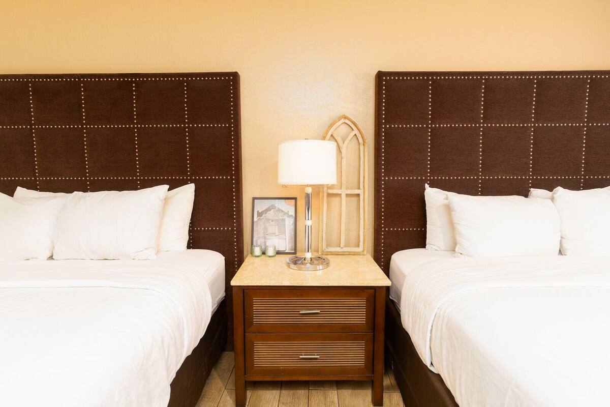 A hotel room with two beds, a nightstand with a lamp, and a framed picture on the wall.