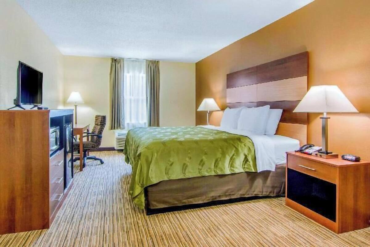 Une chambre d’hôtel comprenant un lit, deux lampes de chevet, un bureau avec une chaise, une télévision et un mini-bar.