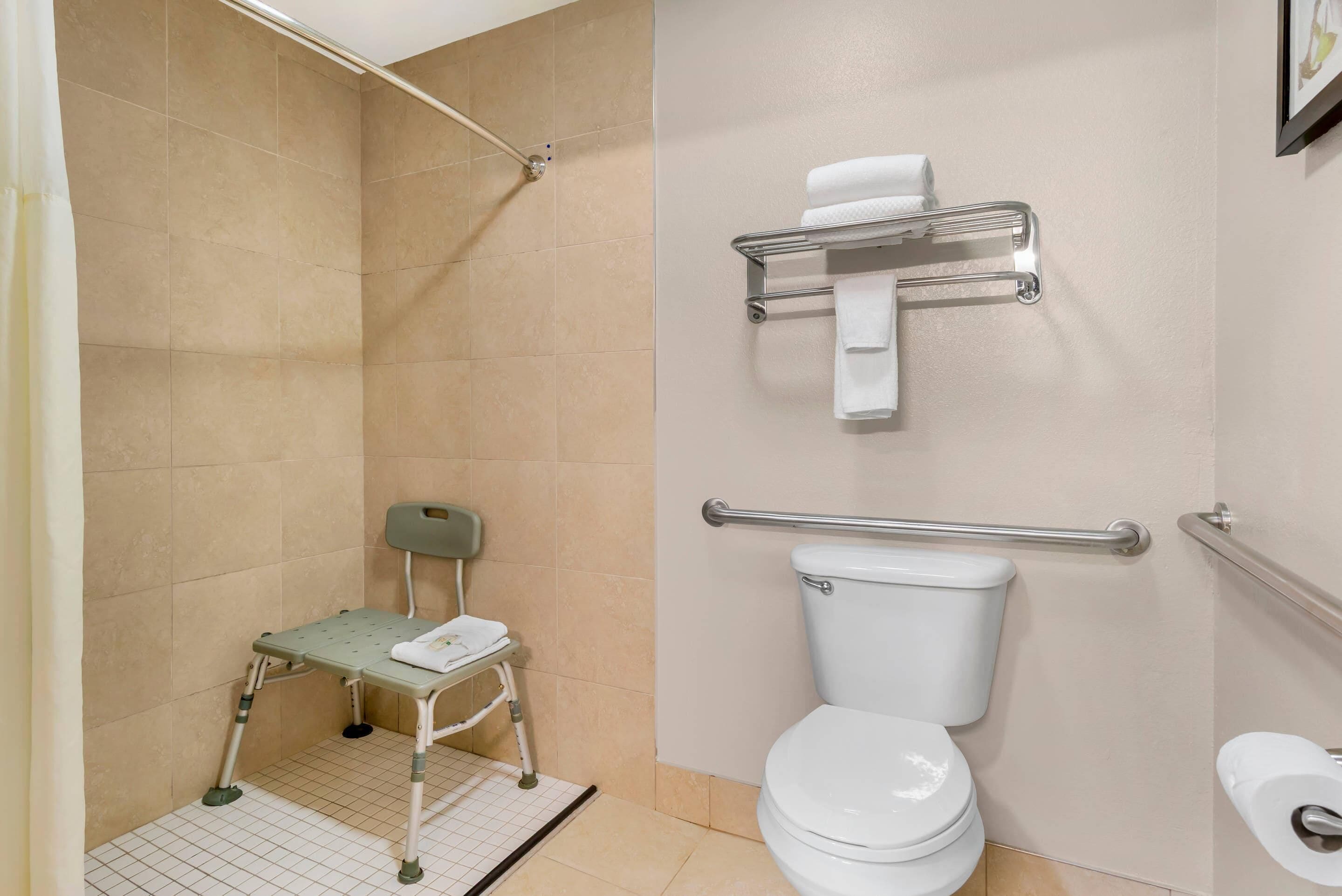 A bathroom with a shower, toilet, grab bars, a towel rack, and a wheelchair.