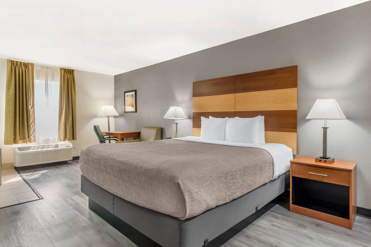 Une chambre d’hôtel moderne avec un grand lit, des tables de chevet avec des lampes, une chaise et une fenêtre avec des rideaux.