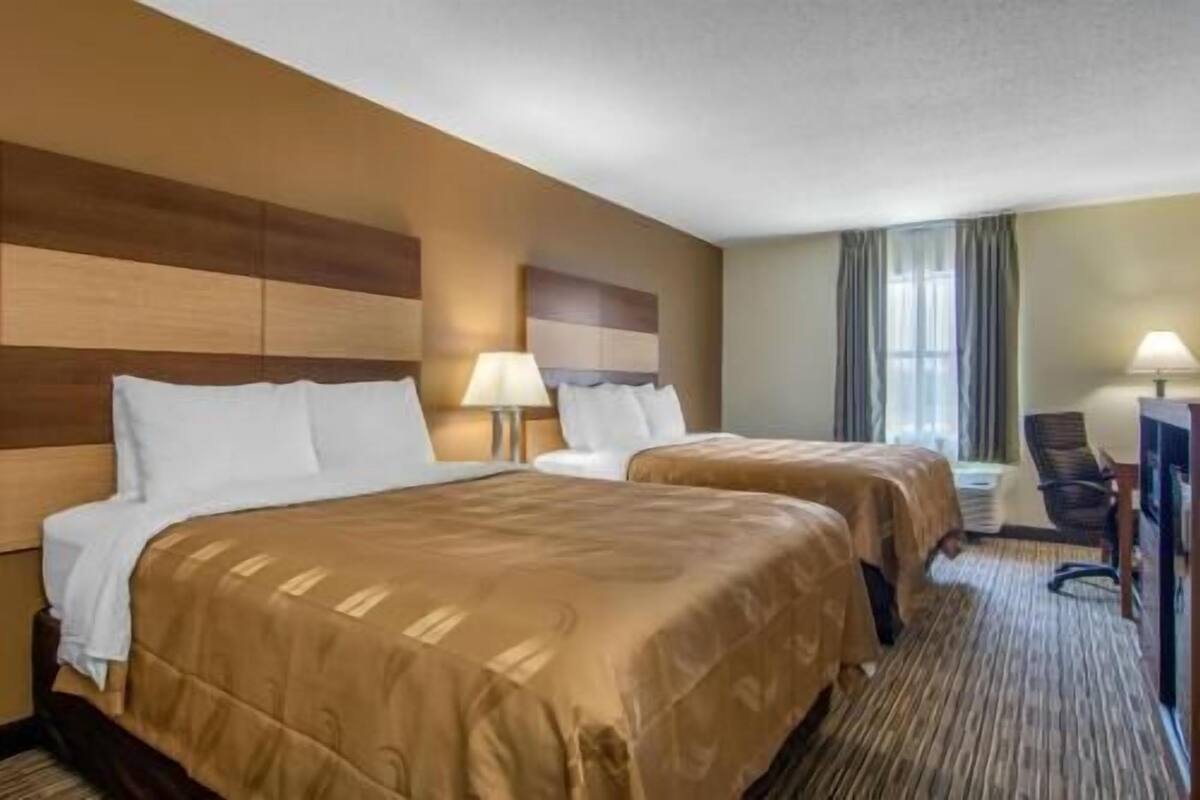 Une chambre d’hôtel avec deux lits, un bureau, une chaise et une fenêtre avec des rideaux.