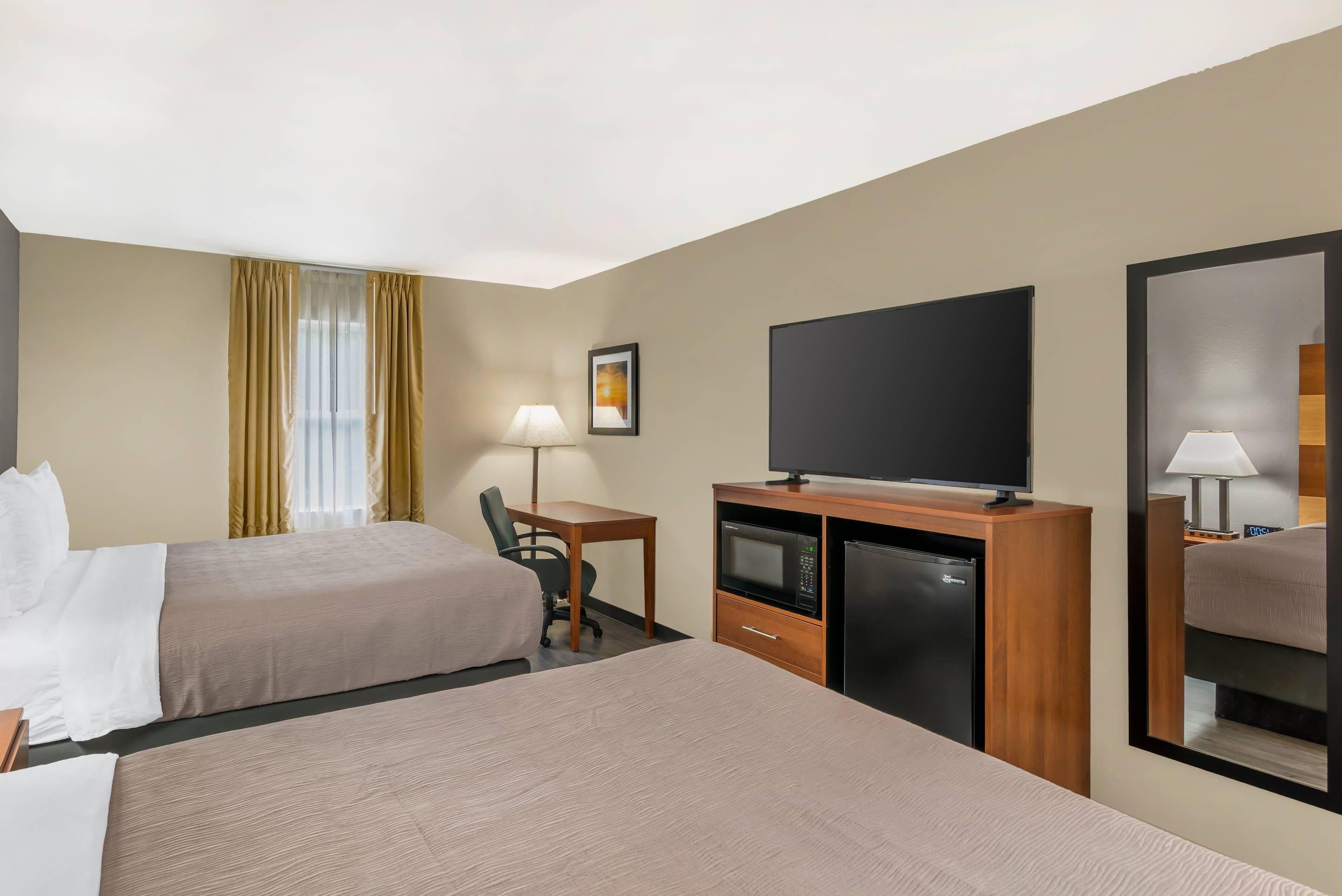 Habitación de hotel con dos camas, un escritorio con silla, televisión, microondas y refrigerador.