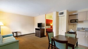 A hotel room with a kitchenette, a dining area with a table and chairs, a TV, a bed with a red blanket, and a lamp. - Econo Lodge Inn & Suites Clearwater Central (Clearwater)