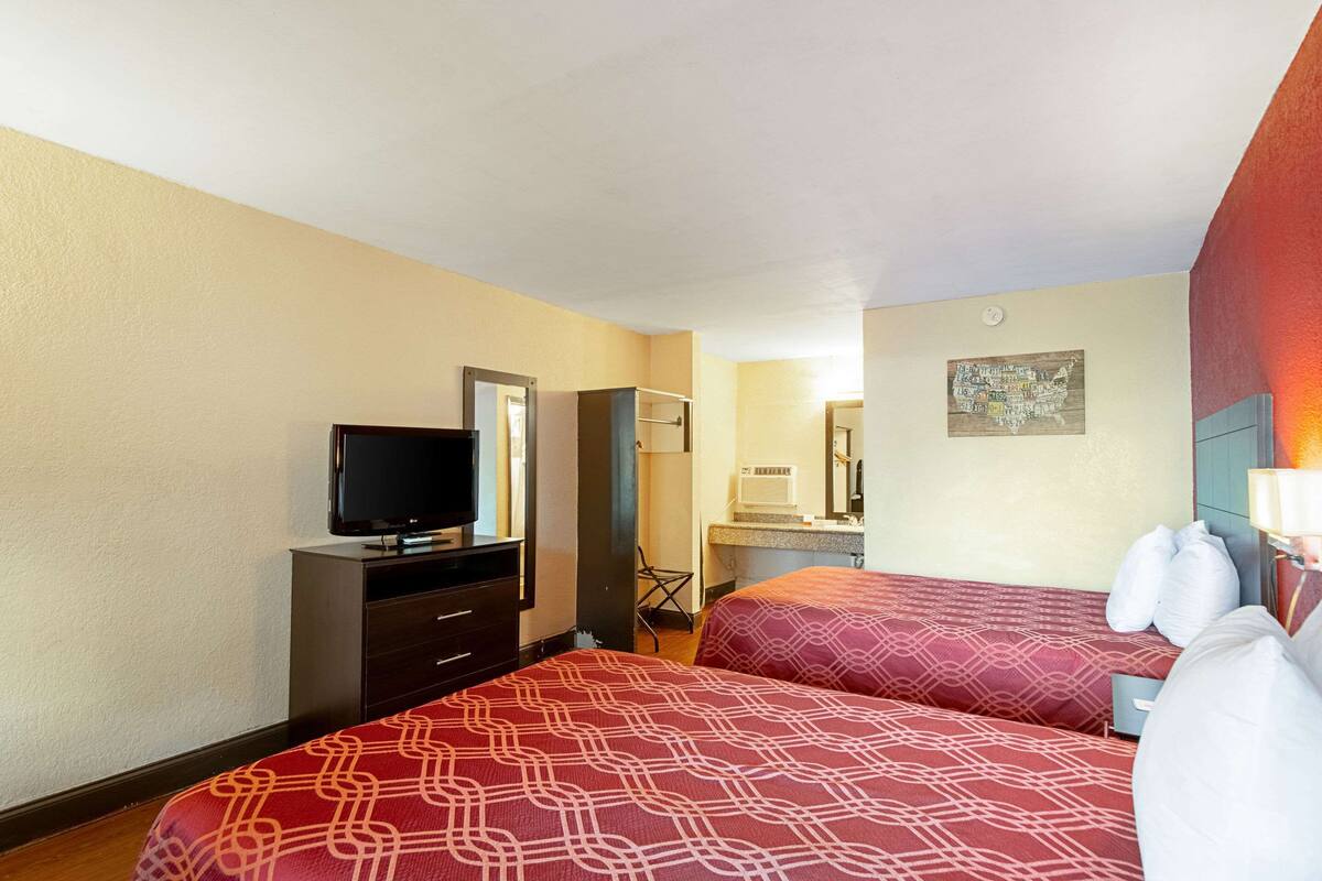 A hotel room with two beds, a TV, a desk, and a bathroom visible in the background.