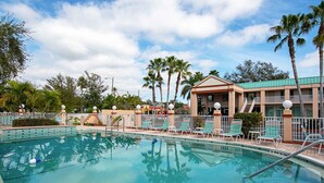 A swimming pool with lounge chairs and palm trees, surrounded by a building with a green roof. - Econo Lodge Inn & Suites Clearwater Central (Clearwater)