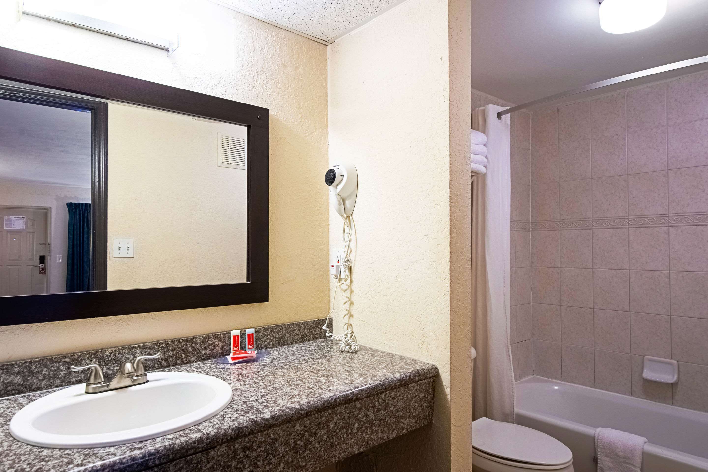 A bathroom with a granite countertop, a white sink, a mirror, a hairdryer, and a bathtub.