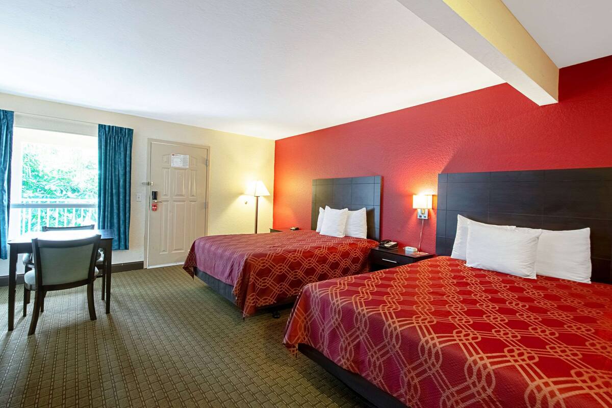 A hotel room with two beds, a desk, and a window with curtains.