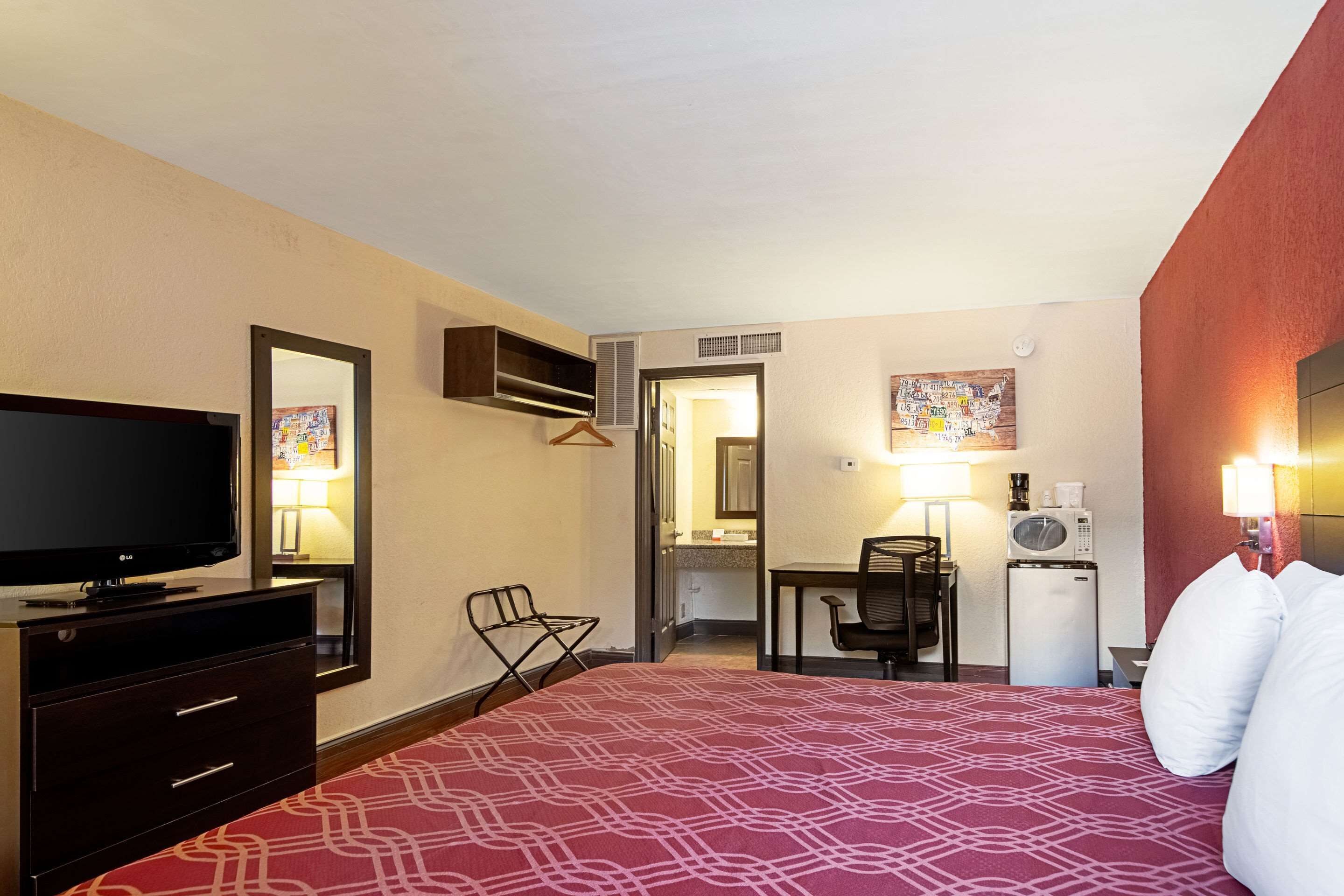 A hotel room with a bed, a TV, a desk, a chair, a microwave, and a refrigerator.