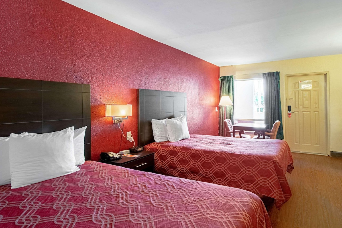 Quarto de hotel com duas camas, cabeceira, mesas de cabeceira, escrivaninha e uma cadeira.