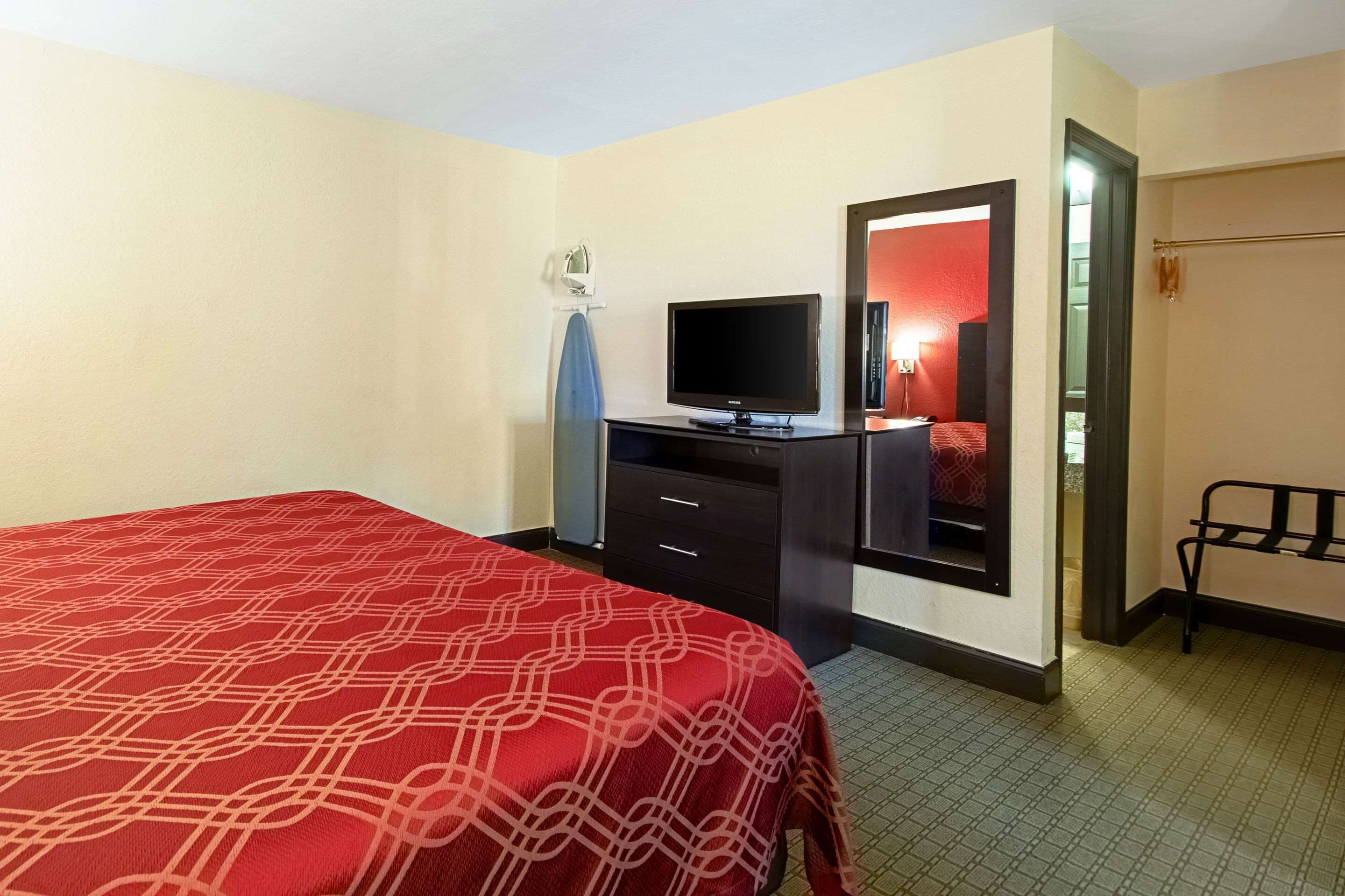 Quarto de hotel com uma cama, televisão em uma cômoda, espelho e porta que dá para outro quarto.