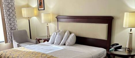 A hotel room with a large bed, two bedside tables, a chair, and a lamp.