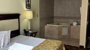 A hotel room with a bed, a bedside lamp, a telephone, a bathroom with a bathtub, and a towel rack. - Baymont by Wyndham Johnson City (Johnson City)