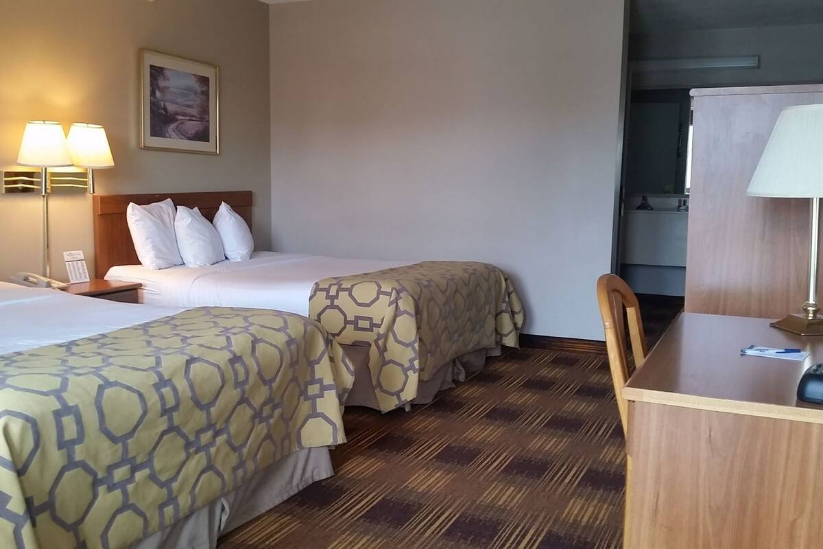 A hotel room with two beds, a desk, a chair, a lamp, and a painting on the wall.