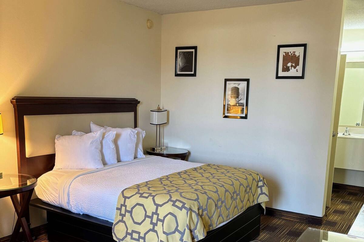 A hotel room with a bed, bedside tables, a lamp, and two framed pictures on the wall.