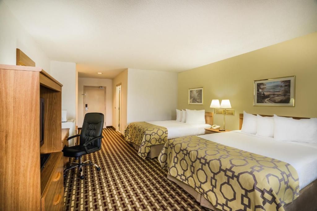 A hotel room with two beds, a desk, a chair, and a patterned carpet.