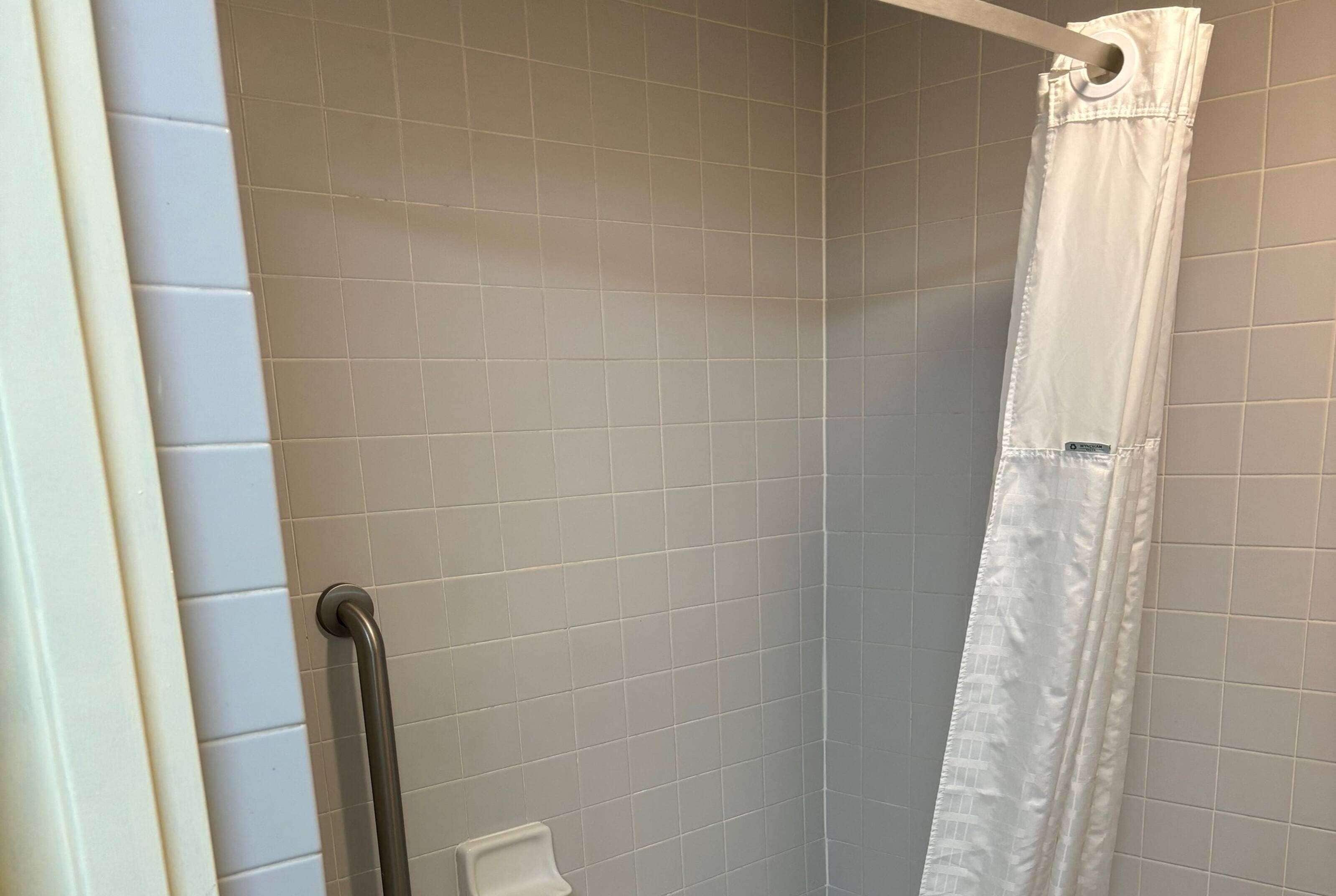 A shower with a white curtain, tiled walls, and a grab bar.