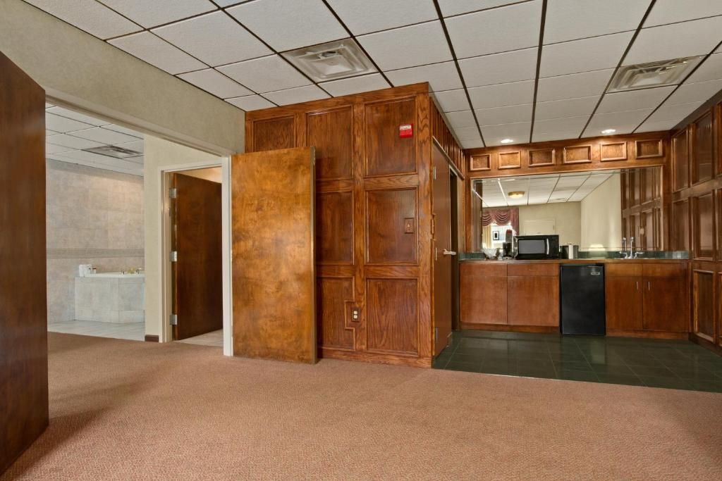 A hotel room with a large wooden wardrobe, a kitchenette with a microwave, and a bathroom visible through an open door.