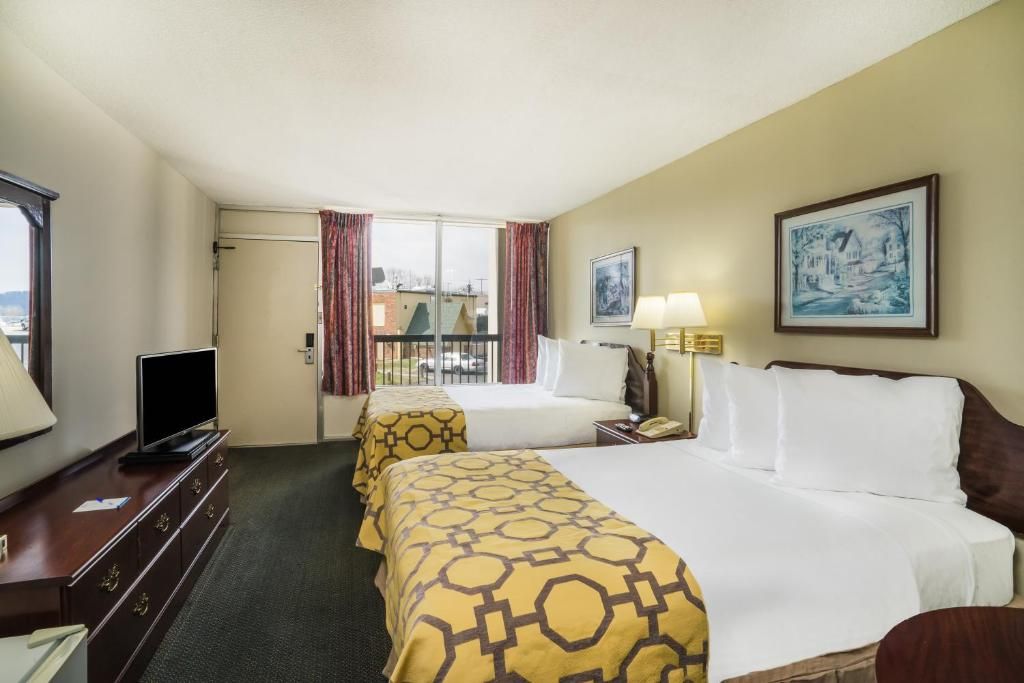 Habitación de hotel con dos camas, televisión, escritorio y ventana con cortinas.