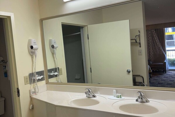A hotel bathroom with two sinks, a large mirror, and a hairdryer mounted on the wall.