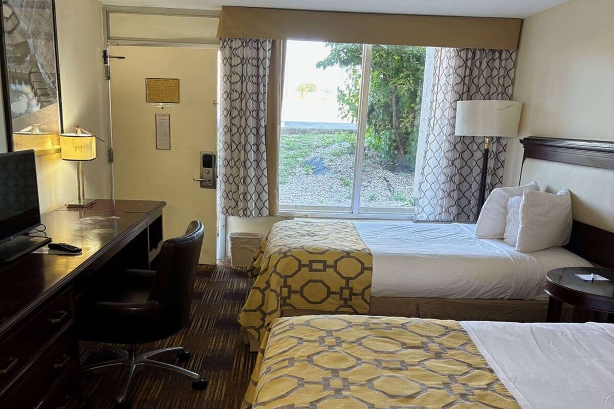 A hotel room with a bed, desk, chair, and a window with curtains.