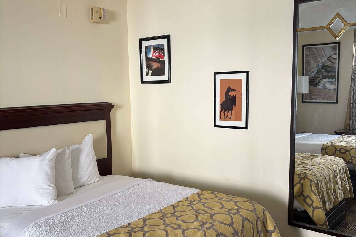 A hotel room with a bed, a headboard, and two framed pictures on the wall.