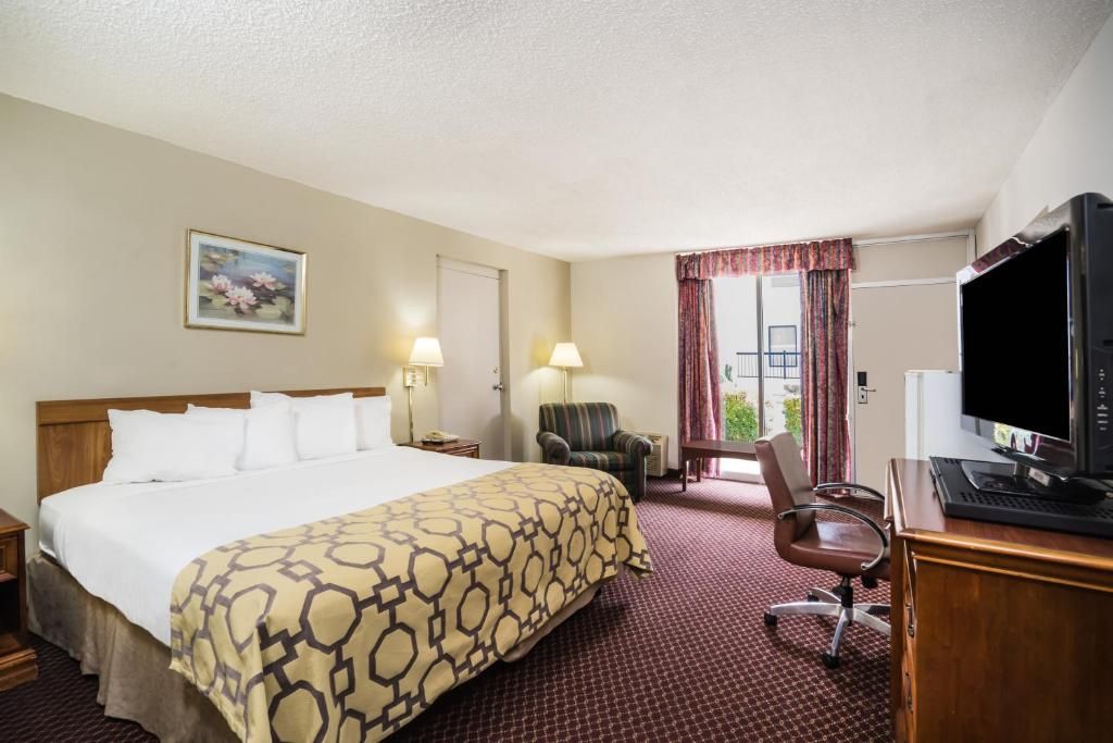 A hotel room with a bed, a desk with a computer, a chair, a television, and a window with curtains.