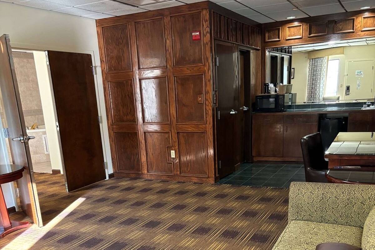 A hotel room with a wooden wardrobe, a dining area with a table and chairs, and a kitchenette with a microwave.