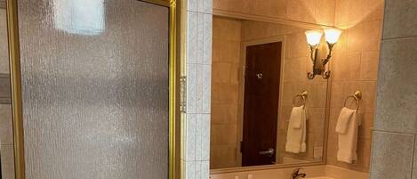 A bathroom with a large mirror, two wall-mounted lights, a sink, and a door with a frosted glass panel.
