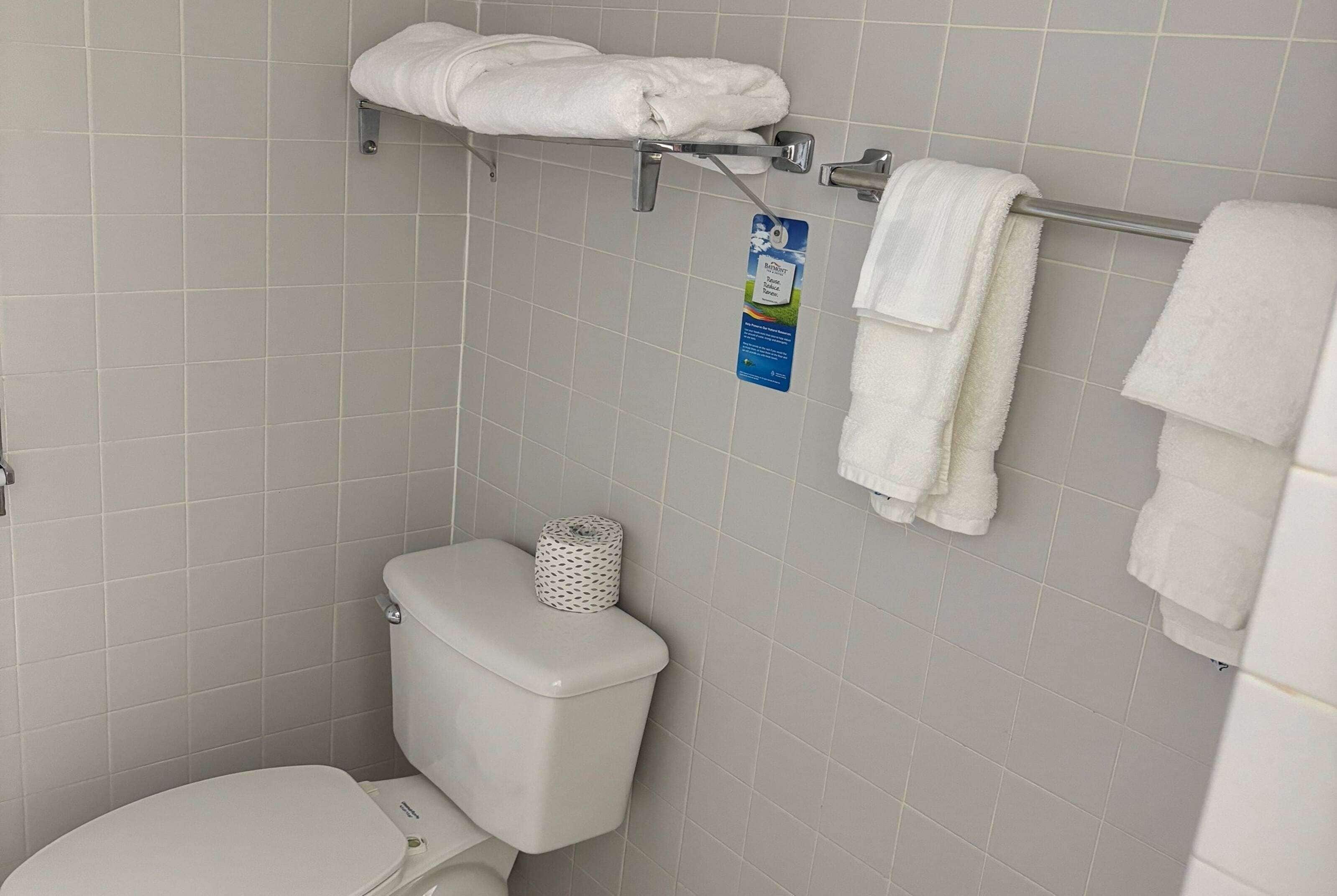 Un baño con inodoro, toallero con toallas dobladas y dispensador de papel higiénico.